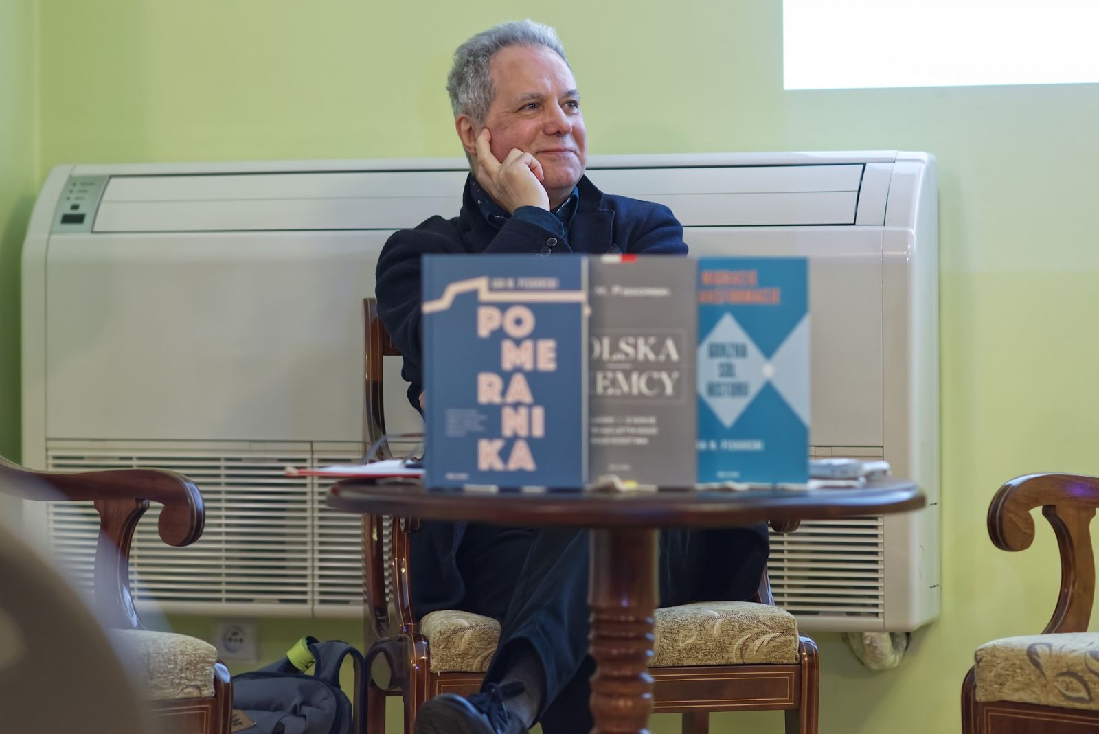 Profesro Jan Piskorski siedzi, na pierwszym planie książki stoja na stoliku