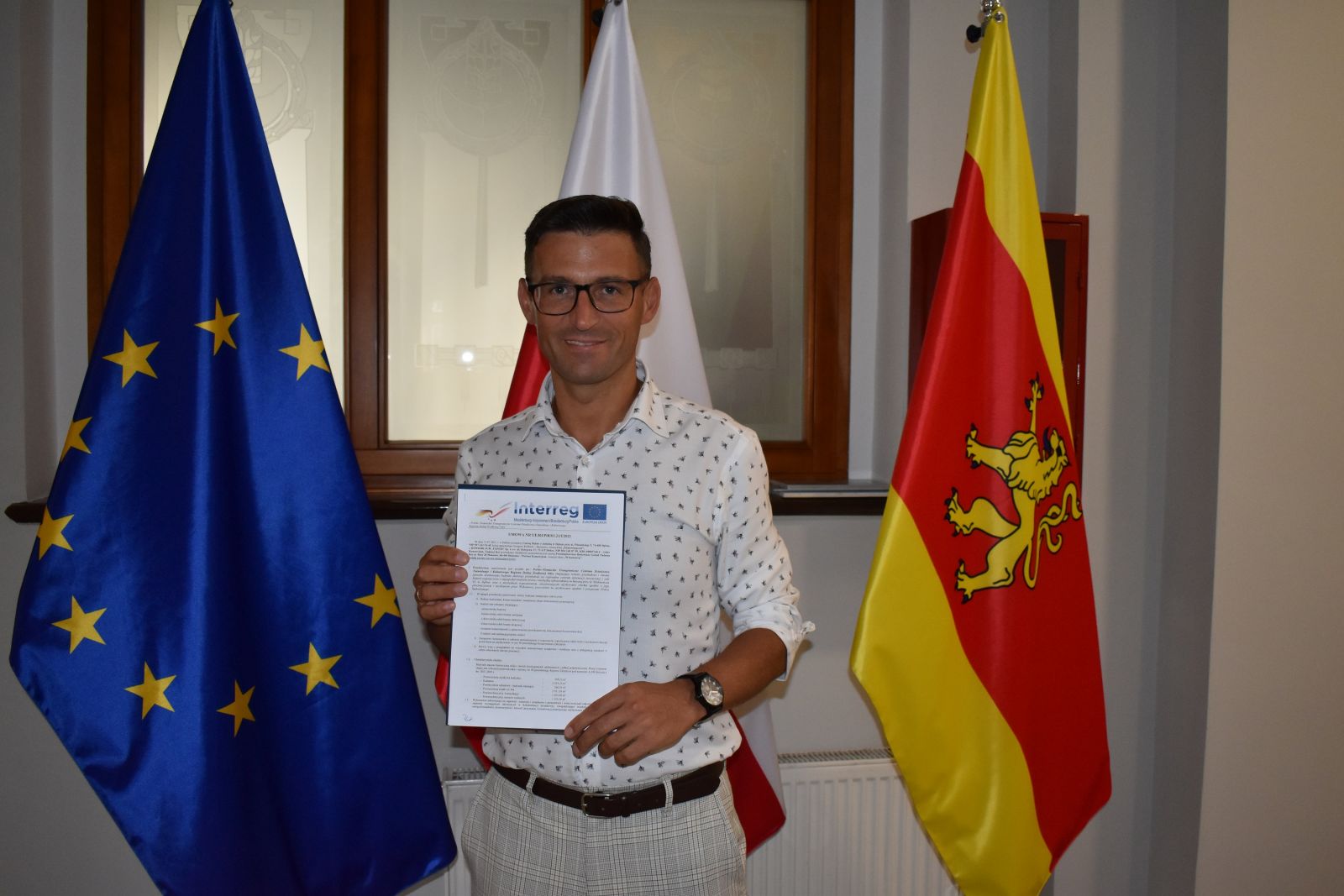 Burmistrz Dębna na tle flag UE i Dębna pokazuje podpisaną umowę 