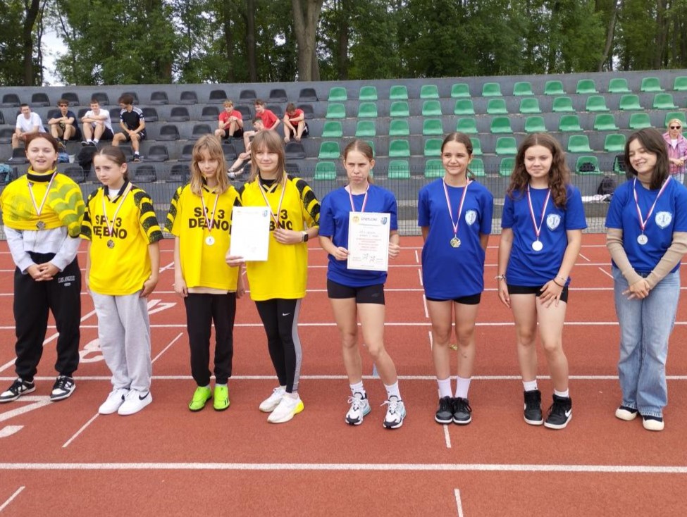 od prawej zwycięski zespół dziewcząt w niebieskich koszulkach koszulkach, obok zspół dziewczat w żółtych koszulkach stoja na bieżni 
