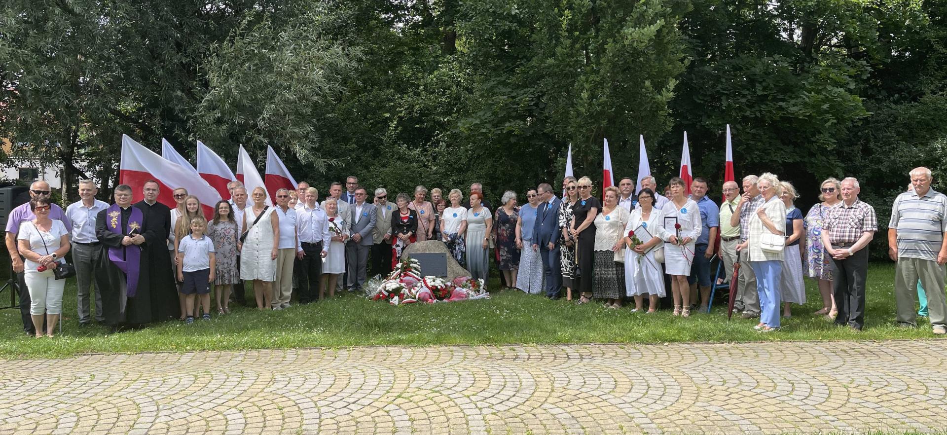 Uczestnicy uroczystości stoją wokół Głazu  Pamięci. 