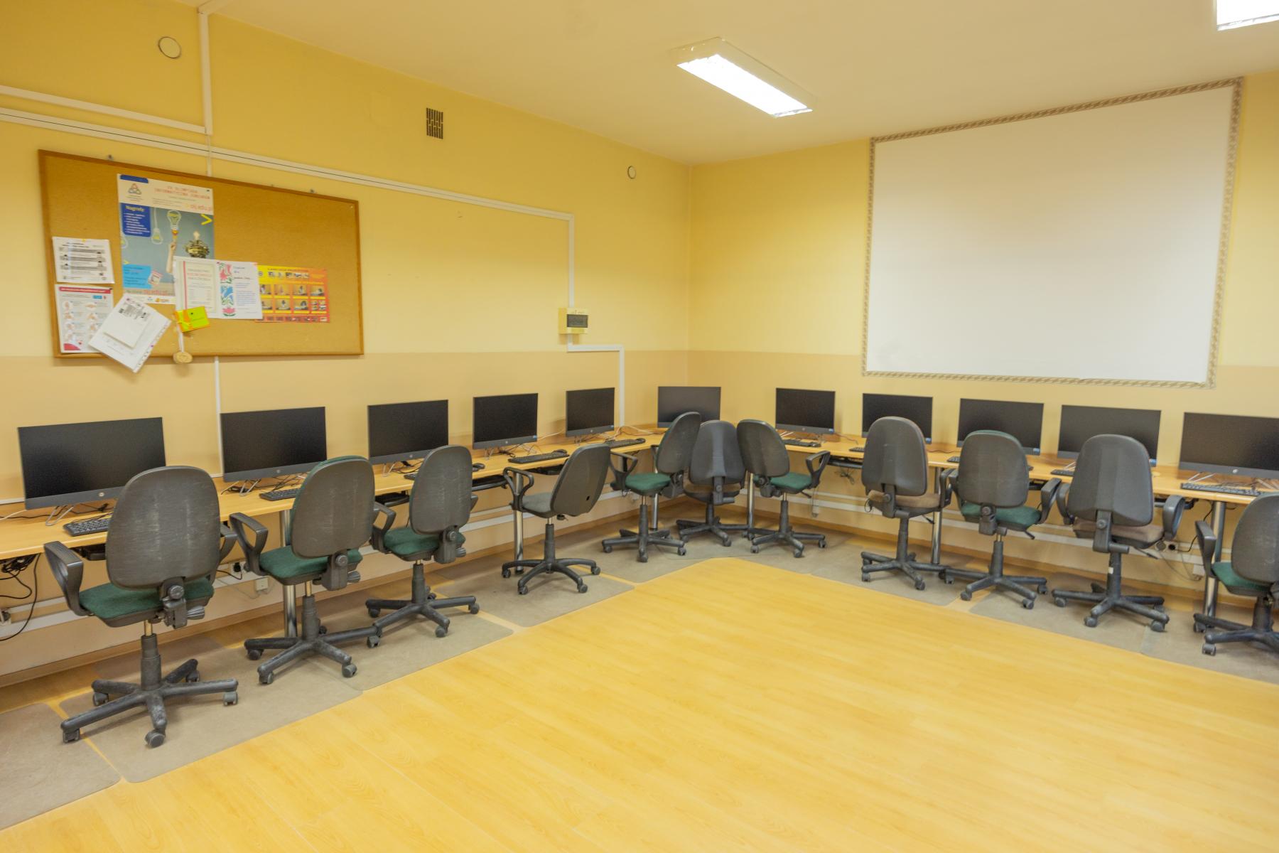 Pracownia komputerowa w szkole. sala pomalowana na żółto, do okoła przy ścianach ławki, krzesła i monitory