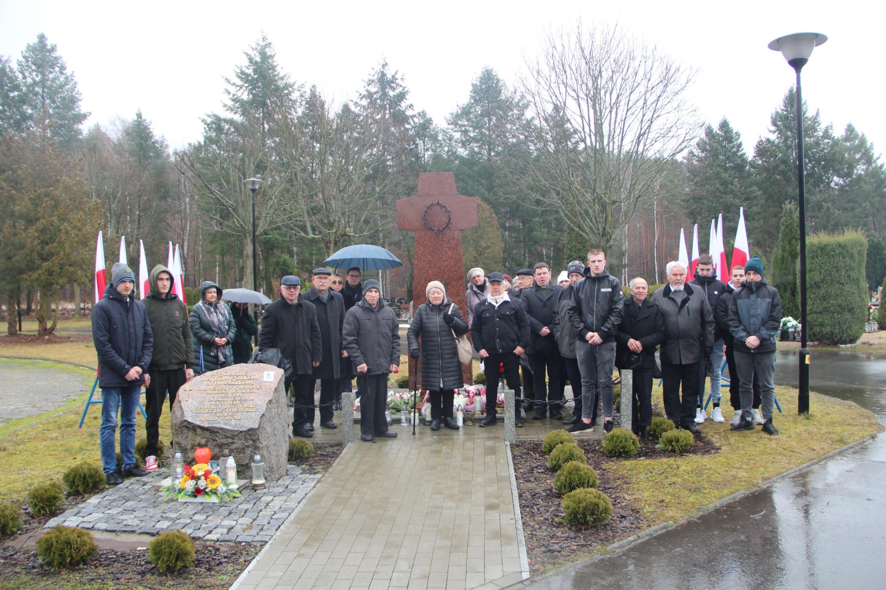 Grupa uczestników uroczystości przed Pomnikiem Sybiraka. W tle flagi Polski 