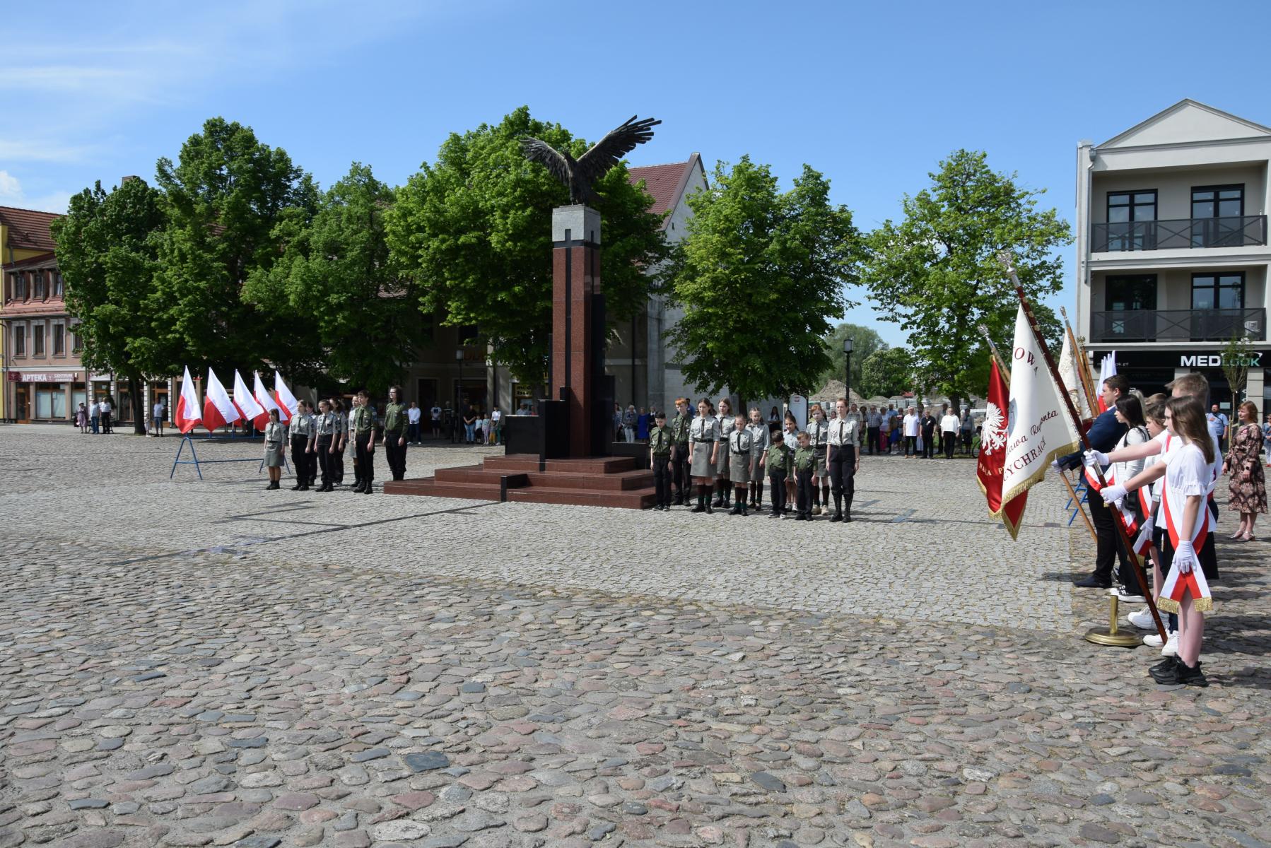 Przy pomniku Orła Białego po bokach stoją harcerze, po lewej poczty sztandarowe ze szkół