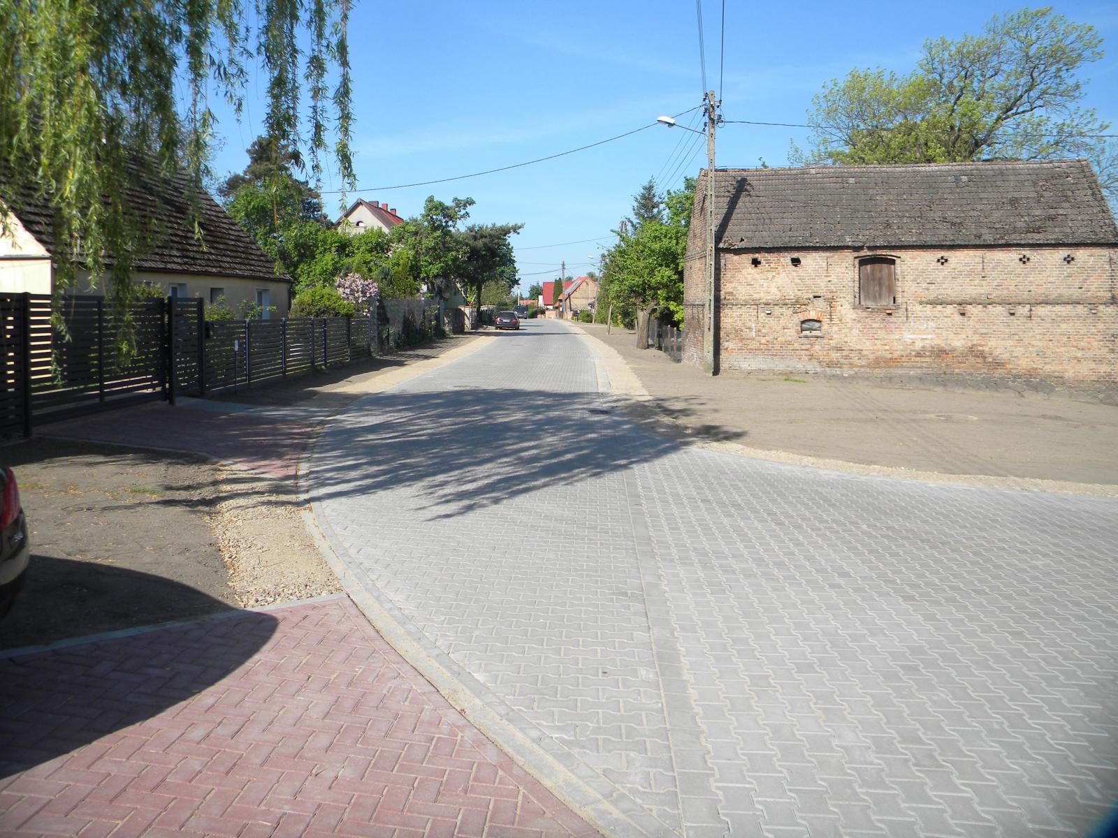 Droga zrobiona szarej kostki polbrukowej, po bokach budynki
