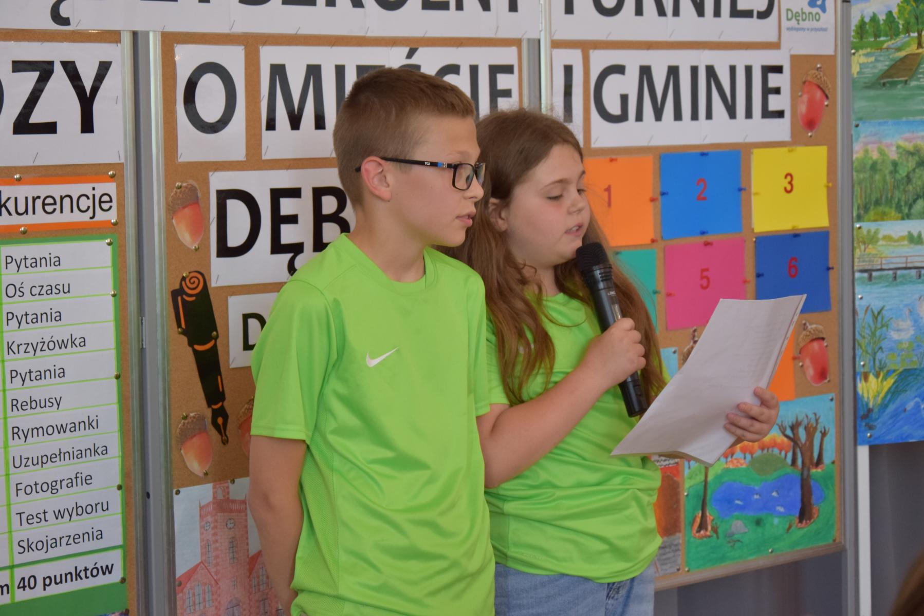 Uczeń i uczennica z SP Sarbinowo stoją. Dziewczynka z mikrofonem czyta na białej kartce