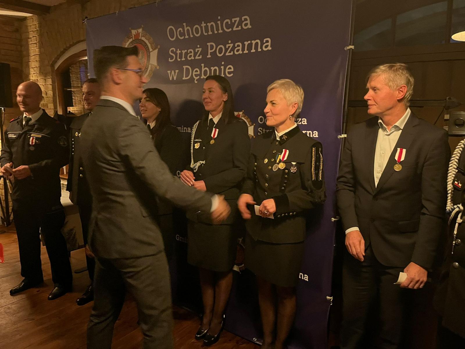 Stoi grupa osób kobiet i mężczyzn w mundurach, która otrzymała medale. Gratulacje składa burmistrz Dębna