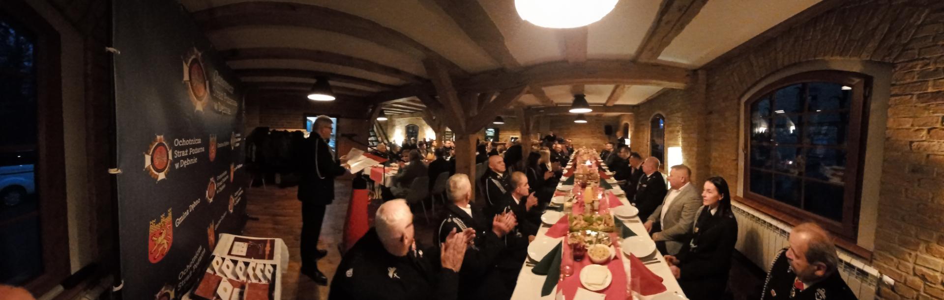 Widok na salę, przy stołach siedzą osoby w mundurach, przy mównicy stoi prezes Tadeusz Nowak 