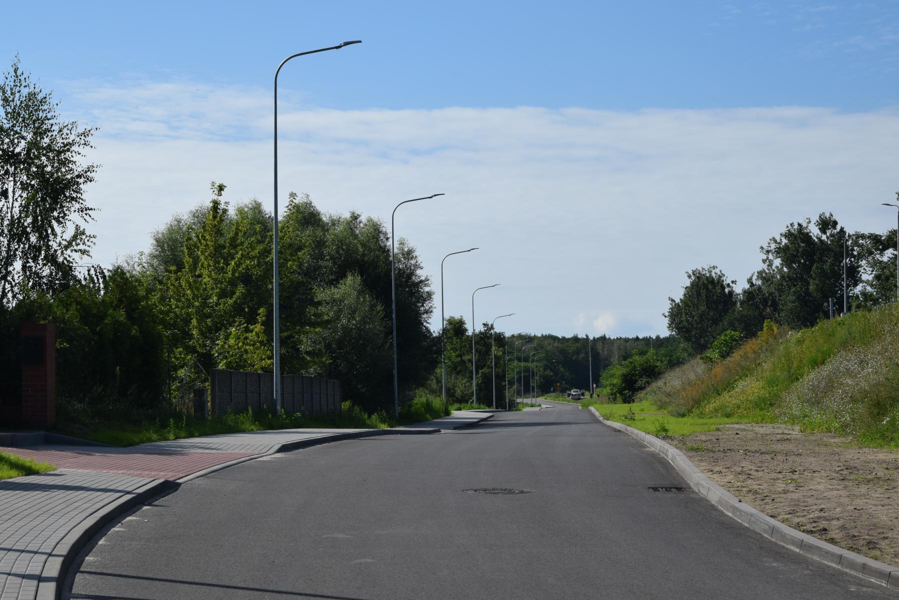 Droga asfaltowa, chodnik jednostronny lampy, zieleń. Ulica Kolejowa 