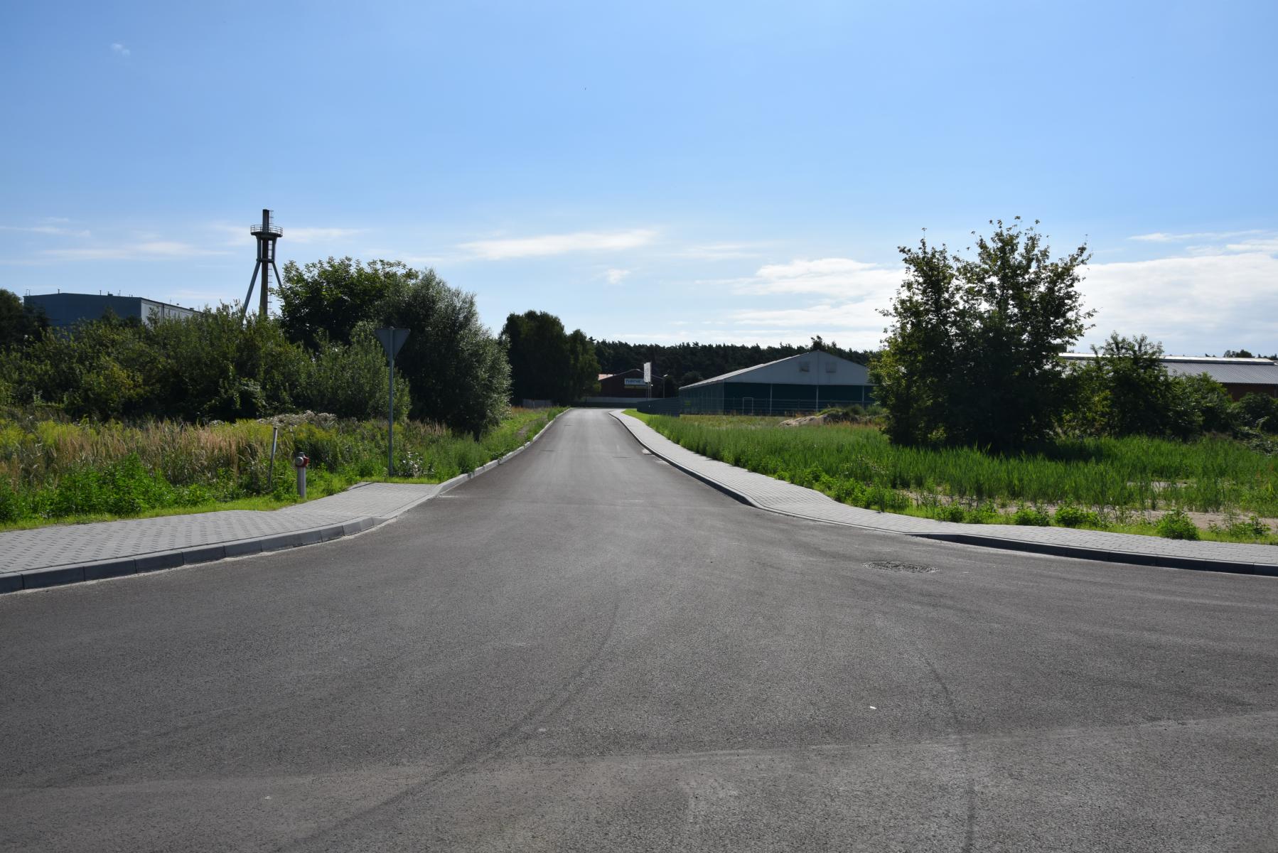 Ulica Usługowa, jezdnia asfaltowa, chodnik z kostki, zieleń, zakład w oddali